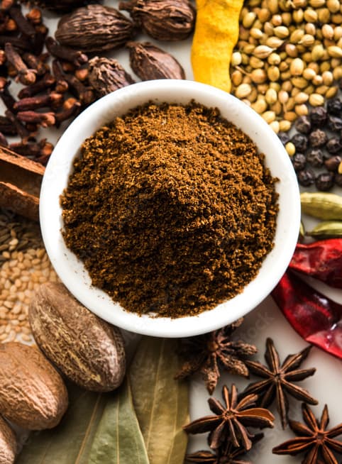 Garam masala in a white bowl with whole spices